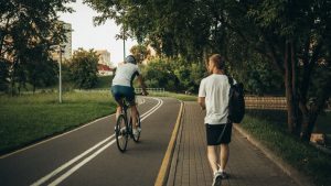A cyclist and a walker enjoy a peaceful park trail surrounded by greenery.